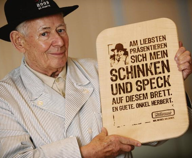 Herbert Ospelt hält ein Holzbrett mit Text hoch